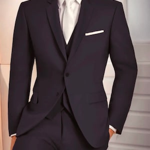May include: A dark blue suit with a white shirt and a white pocket square. The suit jacket has a single button closure and a three-piece design.