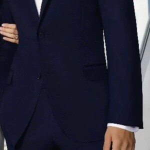 May include: A dark blue suit jacket with a white pocket square. The jacket has a single button closure and a notch lapel.