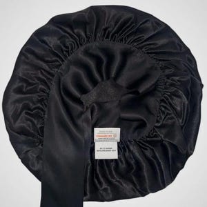 May include: Black silk bonnet with a satin finish. The bonnet has a wide band and a label that reads "STANDARD 100 by OEKO-TEX". The label also states "BA 22 MOME 100% MULBERRY SILK".