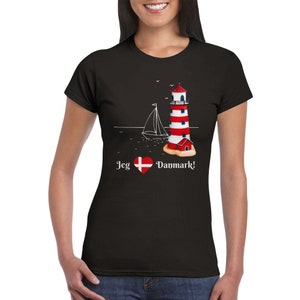 Könnte beinhalten: Schwarzes T-Shirt mit einem weißen Leuchtturm- und Segelboot-Motiv. Der Text "Jeg  Danmark!" ist mit einem roten Herzen und einer dänischen Flagge auf das Shirt gedruckt.