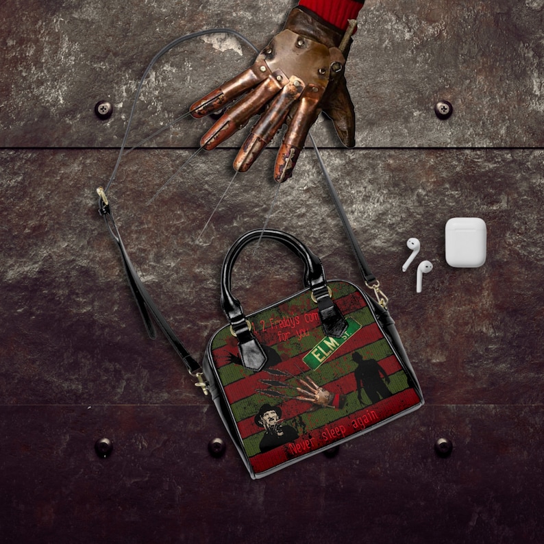 May include: A black handbag with a red, green, and black striped design. The bag features a graphic of Freddy Krueger from the movie "A Nightmare on Elm Street" with the text "Never sleep again".