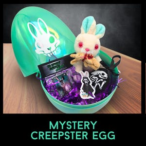 Puede incluir: Un huevo de plástico verde con un diseño de calavera de conejo en la mitad superior, lleno de papel triturado morado, un conejito de peluche y otros artículos misteriosos. El huevo está etiquetado como "MYSTERY CREEPSTER EGG".