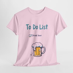 Può includere: Maglietta rosa con il testo "To Do List" e un segno di spunta accanto a "Drink beer". Sotto il testo c'è una boccia di birra disegnata con la schiuma.
