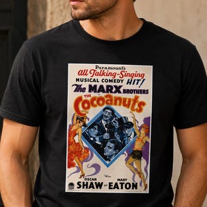 Puede incluir: Una camiseta negra de manga corta con un gráfico de póster de película vintage de The Cocoanuts protagonizada por los hermanos Marx. El estampado incluye texto como Paramount's all Talking-Singing Musical Comedy HIT y Oscar Shaw y Mary Eaton.