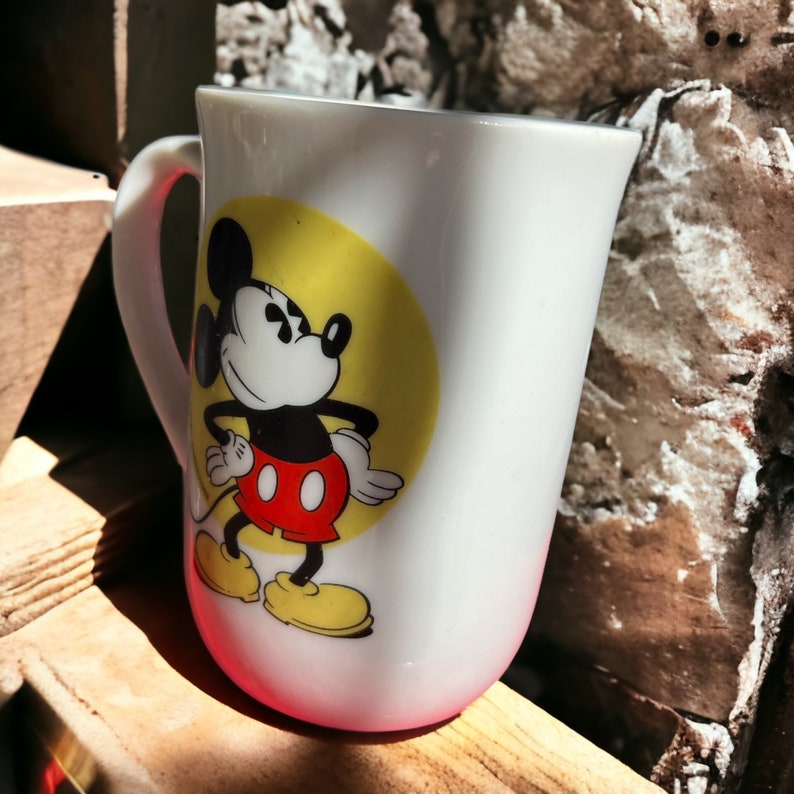 Peut inclure: Une tasse en c&eacute;ramique blanche avec une image de dessin anim&eacute; de Mickey Mouse en short rouge et chaussures jaunes. Mickey est debout sur un cercle jaune avec un contour blanc.