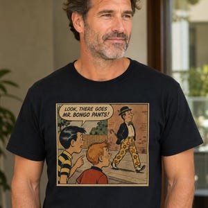 May include: A black t-shirt featuring a vintage comic book illustration of two children pointing at a man walking by. The man wears a dark jacket, a bowler hat, and yellow pants with a floral pattern. The speech bubble reads: LOOK, THERE GOES MR. BONGO PANTS!