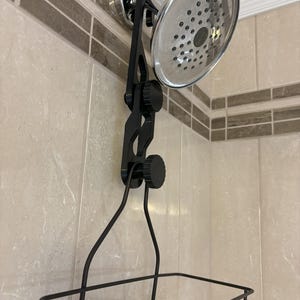 May include: A chrome shower head with a black adjustable arm and a black wire basket for storage. The shower head is mounted on a tiled wall with a decorative border.