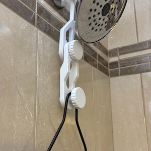 May include: White plastic shower head holder with three adjustable knobs. A black metal shower caddy is hanging from the holder.