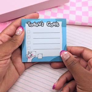May include: A blue and white sticky note with the text "Today's Goals" and a checklist with five blank lines. A cartoon character is in the bottom left corner of the note.