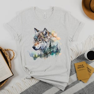 May include: A grey t-shirt with a watercolor design of a wolf's head surrounded by trees and foliage.