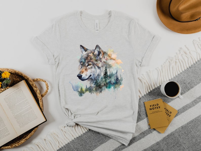 May include: A grey t-shirt with a watercolor design of a wolf's head surrounded by trees and foliage.
