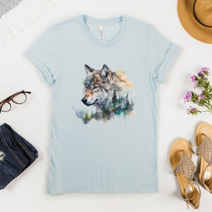 May include: A light blue t-shirt with a watercolor design of a wolf's head with a forest background.