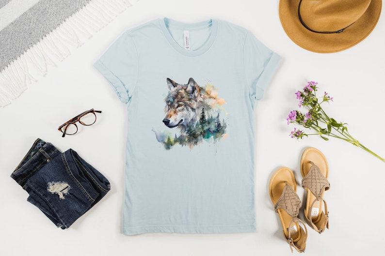 May include: A light blue t-shirt with a watercolor design of a wolf's head with a forest background.