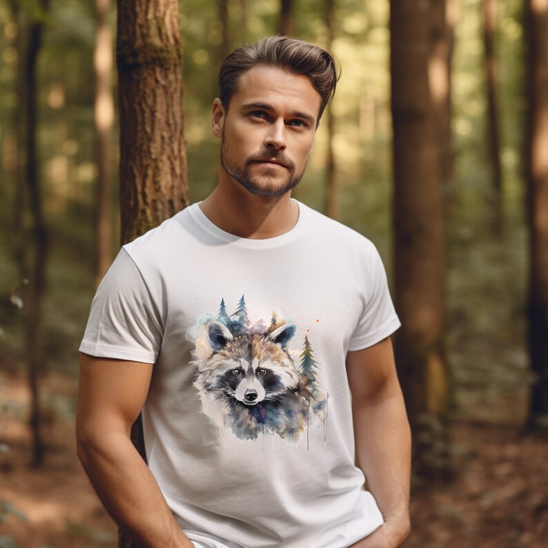 Puede incluir: Camiseta blanca con un dise&ntilde;o de mapache en acuarela y elementos forestales. El mapache est&aacute; representado en tonos grises, marrones y azules, con &aacute;rboles verdes. La camiseta est&aacute; hecha de un material suave y c&oacute;modo.