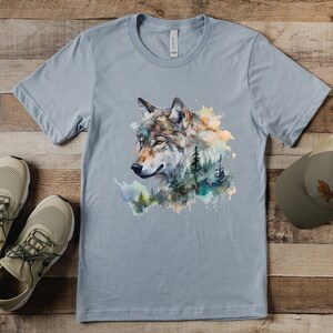 May include: A light blue t-shirt with a watercolor design of a wolf's head surrounded by trees and foliage.