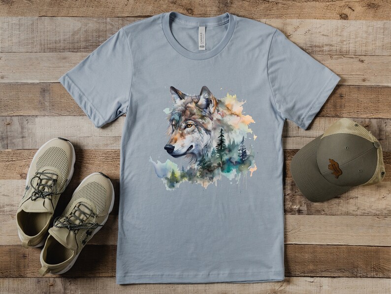 May include: A light blue t-shirt with a watercolor design of a wolf's head surrounded by trees and foliage.