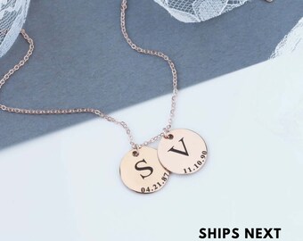 May include: A rose gold necklace with two round pendants. The larger pendant has the letter "V" engraved on it with the date "11.10.90". The smaller pendant has the letter "S" engraved on it with the date "04.21.87".