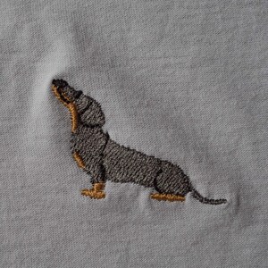 May include: Embroidered dachshund dog design on a white t-shirt.