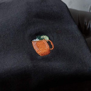 Könnte beinhalten: Schwarzes T-Shirt mit einem gestickten Bild eines Kupferbechers mit einer Limettenscheibe und Eiswürfeln.