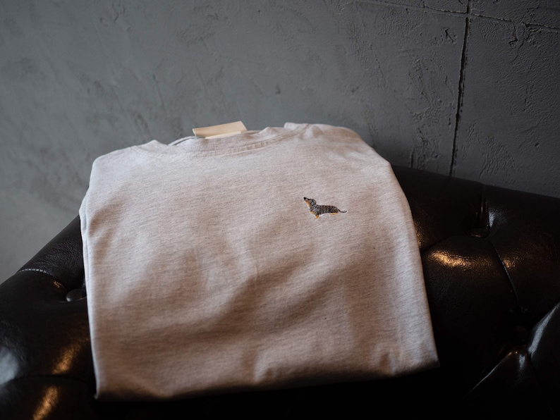 May include: A light gray t-shirt with a small embroidered dachshund on the front.