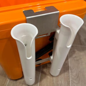 May include: Two white plastic rod holders mounted on a stainless steel bracket attached to an orange cooler.