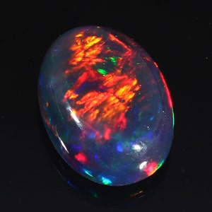 Pu&ograve; includere: Una pietra preziosa di opale nero con un bagliore iridescente rosso, arancione e verde. La pietra di forma ovale &egrave; posizionata su uno sfondo nero.