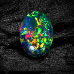 Könnte beinhalten: Ein lebendiger, ovaler schwarzer Opal-Edelstein mit einem faszinierenden Spiel aus grünen, blauen, roten und gelben irisierenden Farben.
