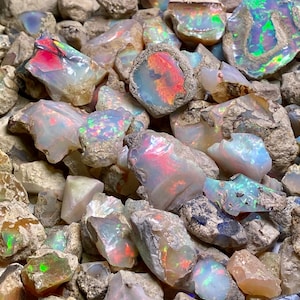 May include: A pile of rough opal stones in various shades of white, grey, and iridescent colours. The stones are mostly opaque with some showing flashes of colour.