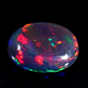 Pu&ograve; includere: Una pietra preziosa di opale nero con taglio a cabochon. L'opale mostra un vibrante gioco di colori con lampi di rosso, verde e blu.