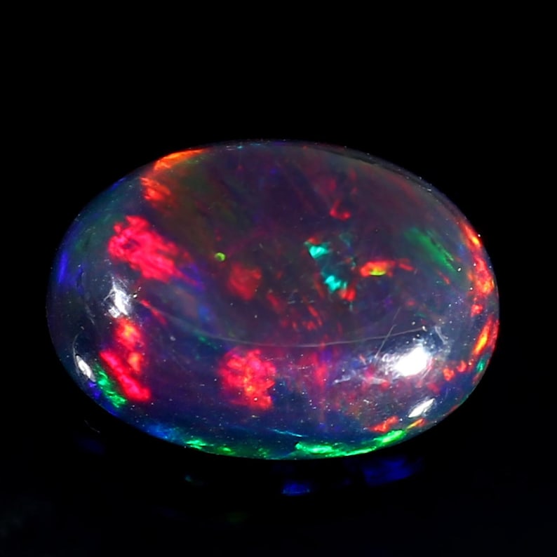 Pu&ograve; includere: Una pietra preziosa di opale nero con taglio a cabochon. L'opale mostra un vibrante gioco di colori con lampi di rosso, verde e blu.