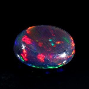 Pu&ograve; includere: Una pietra preziosa di opale nero con riflessi iridescenti rossi, verdi e blu. La pietra di forma ovale &egrave; lucidata e ha una superficie liscia.
