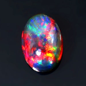 May include: A vibrant black opal gemstone with a fiery red, orange, green, and blue play of colour. The oval-shaped stone is set against a black background.