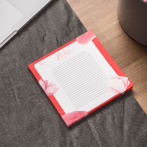 May include: A red notepad with a floral design and the word "Notes" printed on the front. The notepad has lined pages for writing.