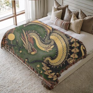 May include: Green and gold dragon throw blanket with a detailed illustration. The blanket features a dragon design with a gold body and a green background. The throw has a fringed edge and is placed on a bed.