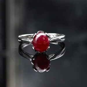 May include: A silver ring with a red ruby gemstone set in a prong setting. The ring has a delicate, twisted band.
