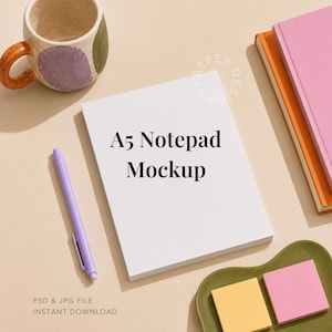 May include: A white A5 notepad mockup with black text reading A5 Notepad Mockup, accompanied by a light purple pen, a ceramic mug with purple and green accents, two stacked notebooks in pink and orange, and two square sticky notes in yellow and pink.