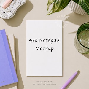 May include: A white rectangular 4x6 notepad mockup centered on a neutral surface. The notepad features the black text 4x6 Notepad Mockup. Surrounding items include a lavender notebook, a light pink pen, a textured white tray, and a green glass.