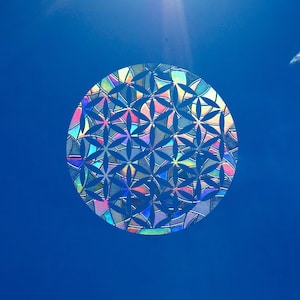 Op de afbeelding: Een holografisch, iriserend levensbloemontwerp tegen een helderblauwe lucht.