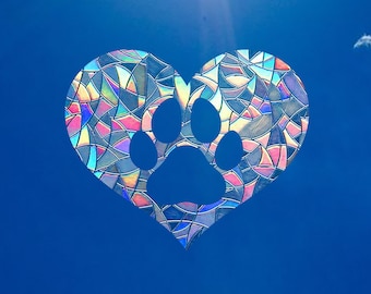May include: A heart-shaped stained glass window with a paw print in the center. The glass is iridescent and reflects a rainbow of colors.