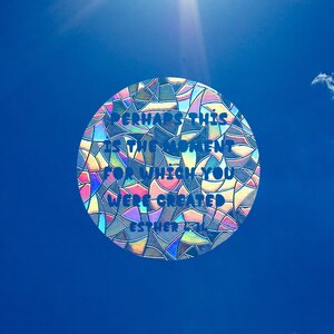May include: A colorful, iridescent, circular sticker with the text "Perhaps this is the moment for which you were created" on a blue sky background.