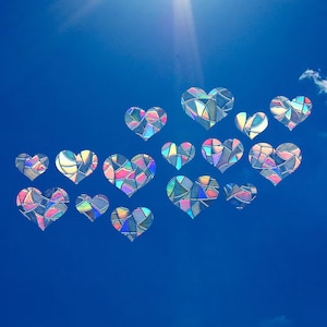May include: A blue sky with a white cloud and a cluster of iridescent heart-shaped decorations. The hearts are made of glass and have a stained glass look.