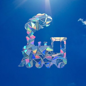 May include: A stained glass silhouette of a train engine against a bright blue sky with a white cloud.