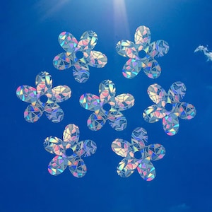 Könnte beinhalten: Sieben regenbogenfarbene holografische Blumenaufkleber vor einem strahlend blauen Himmel.