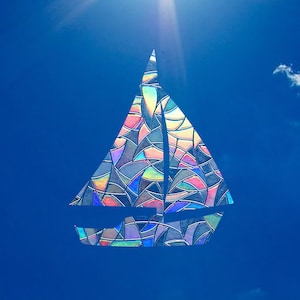 Könnte beinhalten: Eine bunte Silhouette eines Segelboots aus Glasmalerei vor einem strahlend blauen Himmel mit einer weißen Wolke in der oberen rechten Ecke.