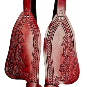 Puede incluir: Par de guardabarros de cuero burdeos para silla de montar con intrincados grabados florales y geométricos. Cada guardabarros tiene una correa de sujeción y un diseño decorativo.