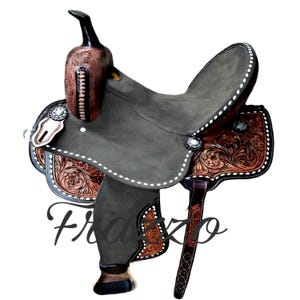 Puede incluir: Una silla de montar de estilo occidental con un asiento gris oscuro y detalles en cuero marrón. La silla presenta intrincados grabados florales, costuras blancas y conchos decorativos plateados. El cuerno es marrón oscuro y los estribos son visibles. La palabra "Frazzo" está escrita en la silla.