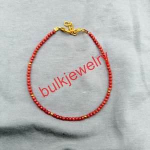 Pode incluir: Uma delicada pulseira de contas com pequenas esferas redondas na cor coral intercaladas com minúsculas contas de metal em tom dourado. A pulseira é fixada com um fecho lagosta de metal dourado e uma pequena corrente extensora no topo.