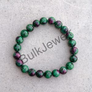 May include: A circular beaded bracelet composed of round, polished stones featuring a mottled pattern of deep forest green and vibrant magenta-pink. The beads are strung together in a continuous loop, displaying natural colour variations throughout.