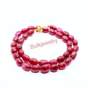 May include: A double-strand necklace composed of polished, oval-shaped deep red beads. The beads are strung together and secured with a gold-toned metal clasp. The text Bulkjewelry is printed in red in the center of the circular arrangement.