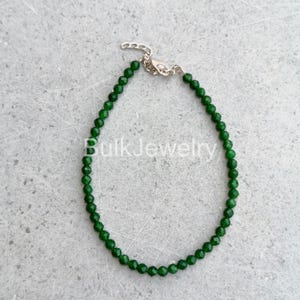 May include: A delicate green beaded bracelet with a silver clasp. The bracelet is made of small, round, faceted beads. The words "Bulk Jewelry" are visible in the image. The bracelet is displayed on a gray surface.